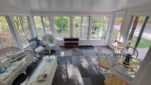 A sunroom with wicker furniture, a fireplace, and large windows overlooking a garden. - Relax at this Private, Peaceful, Dog-Friendly Ecohouse in the Woods. (Lowell)