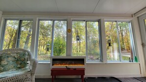 A room with a large window, a fire feature, and a wicker chair. - Relax at this Private, Peaceful, Dog-Friendly Ecohouse in the Woods. (Lowell)