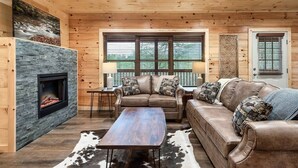 A cozy living room with a stone fireplace, leather sofas, and a large window with blinds. - Best Location 5BR Sleeps 16 (Pigeon Forge)