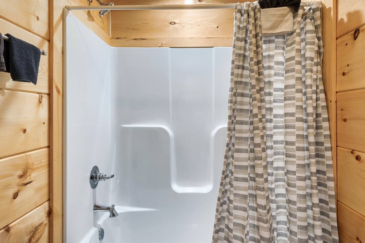 Ein Badezimmer mit Holzwandverkleidung, einer weißen Badewanne, einer Duschvorhang und einem Handtuchhalter.