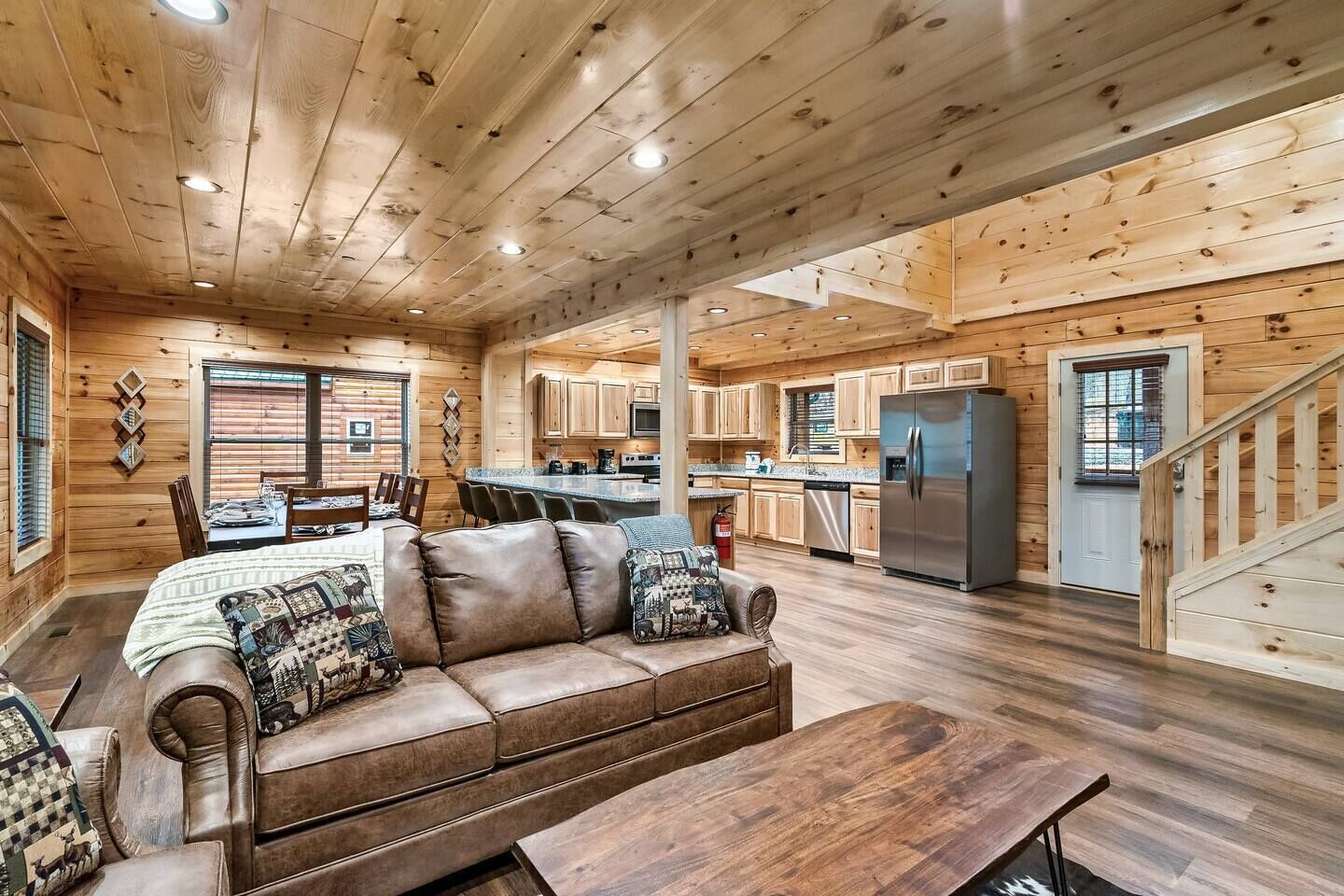 A cabin interior with a wooden floor, a leather sofa, a dining table, and a kitchen area.