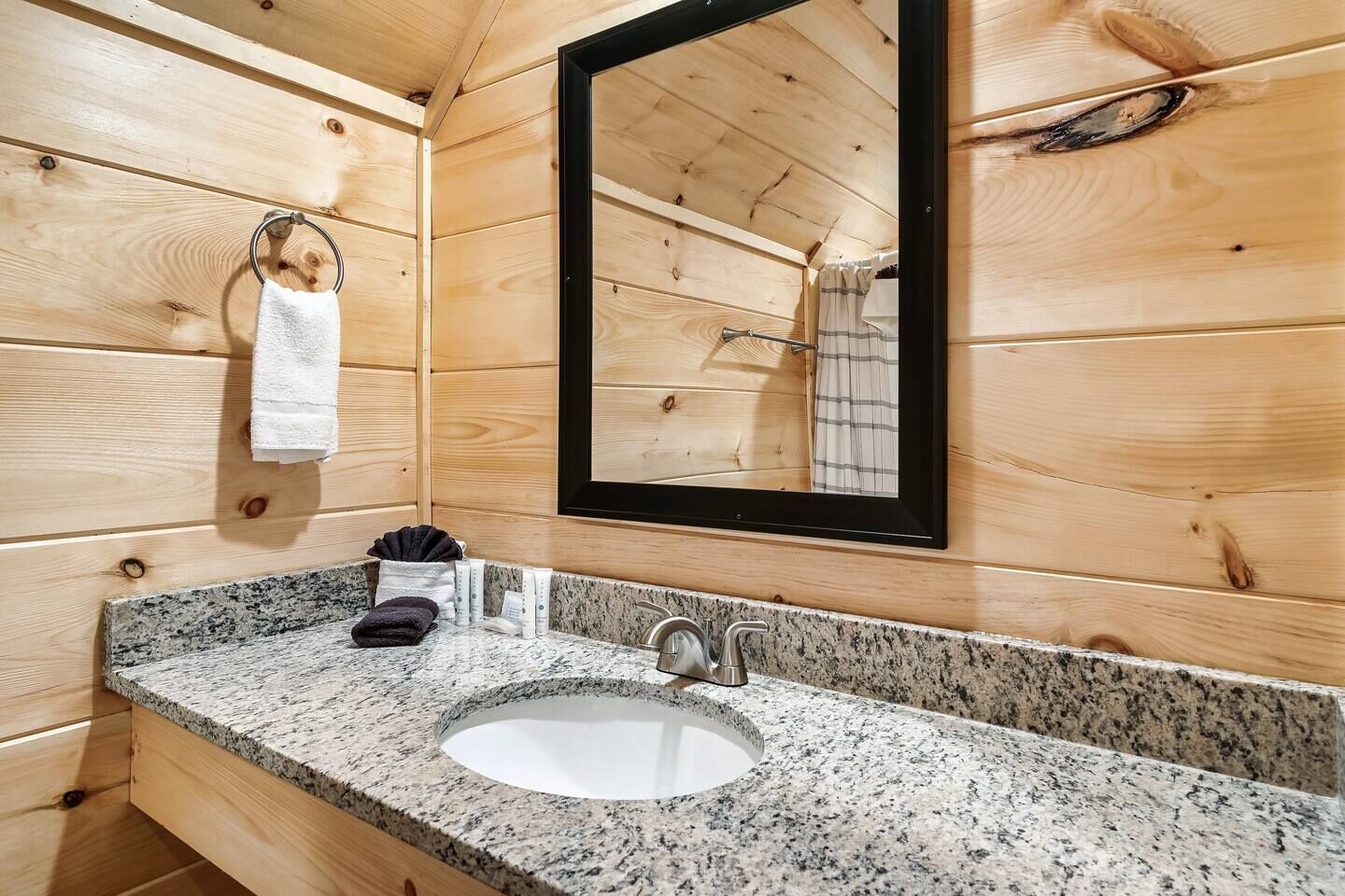 A wooden cabin bathroom with a granite countertop sink, a mirror, and a towel rack.