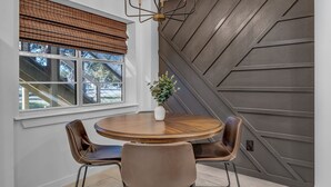 A dining area with a round wooden table, two brown leather chairs, a white vase with a plant, and a window with a brown roller blind. - Modern Lake House 2 Units, Pool, Lake 3Min, Pets (Somerville)