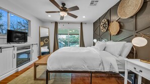 A modern bedroom with a bed, ceiling fan, TV, and a view of the outdoors. - Modern Lake House 2 Units, Pool, Lake 3Min, Pets (Somerville)