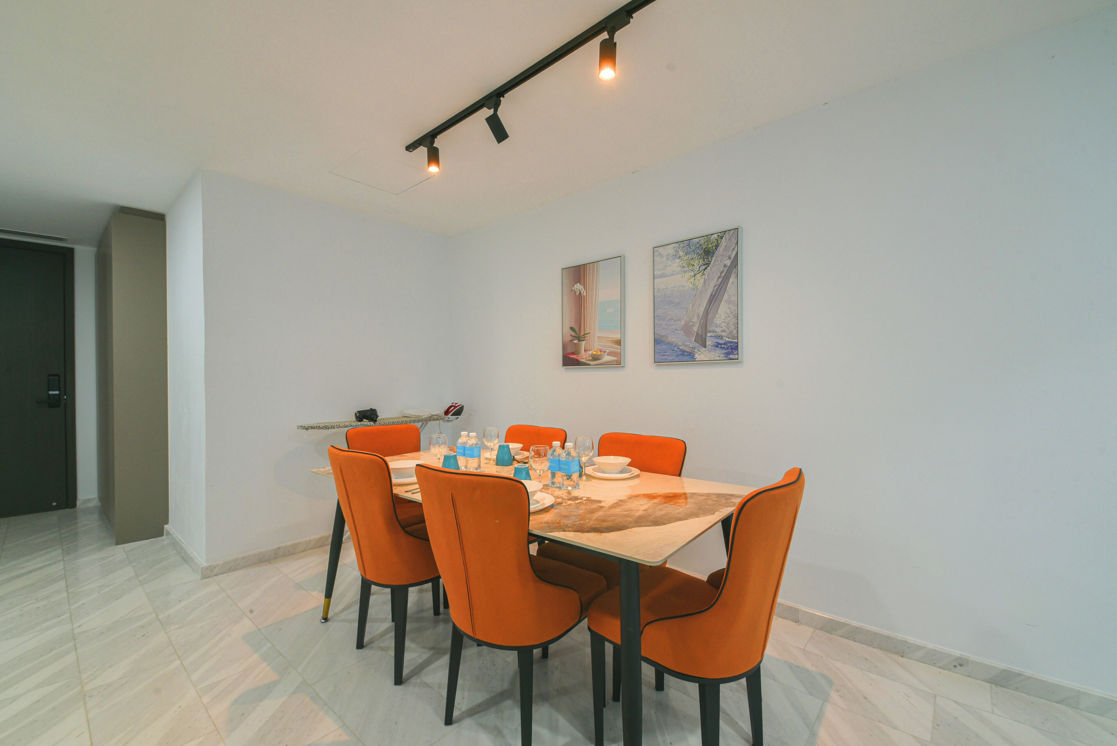 A dining area with a table set for six, orange chairs, and two wall-mounted paintings.