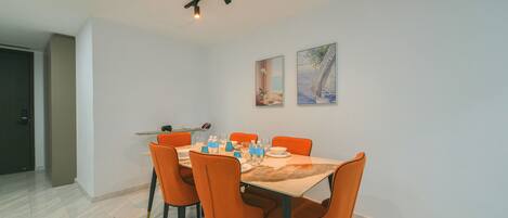 A dining area with a table set for six, orange chairs, and two wall-mounted paintings.