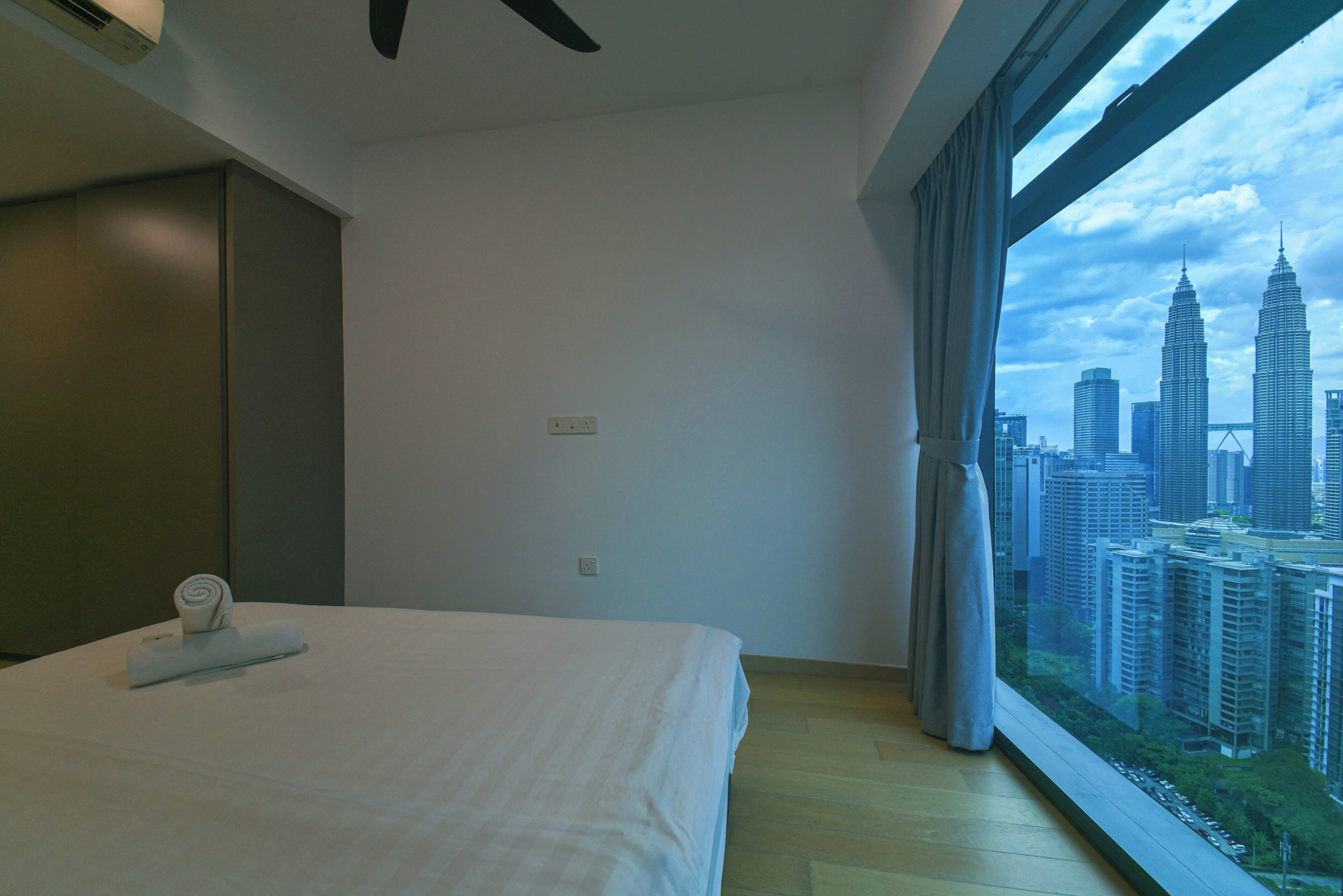 A hotel room with a bed, a window with a city view, and a ceiling fan.