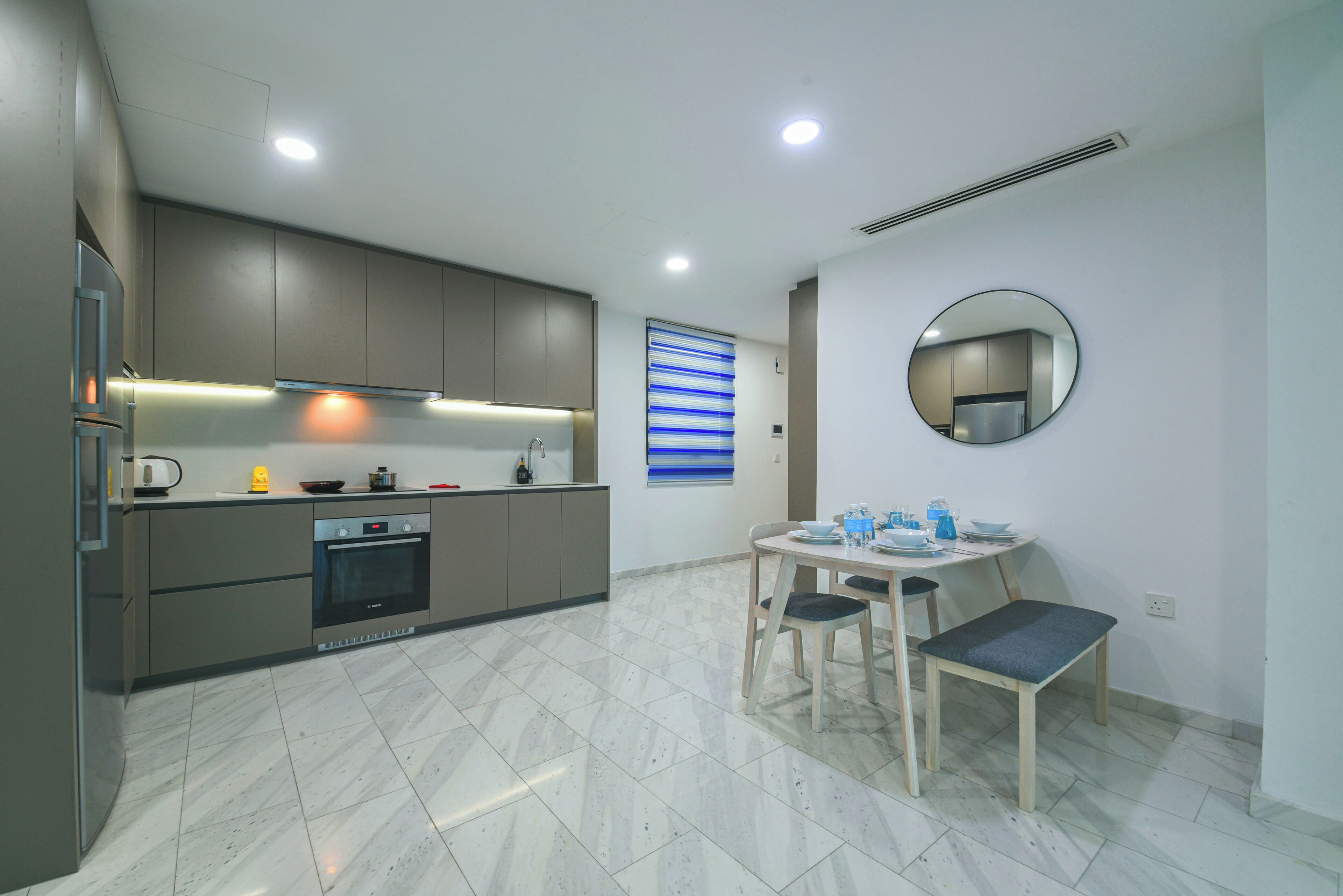 A modern kitchen with grey cabinets, a built-in oven, and a dining area with a round table and chairs.