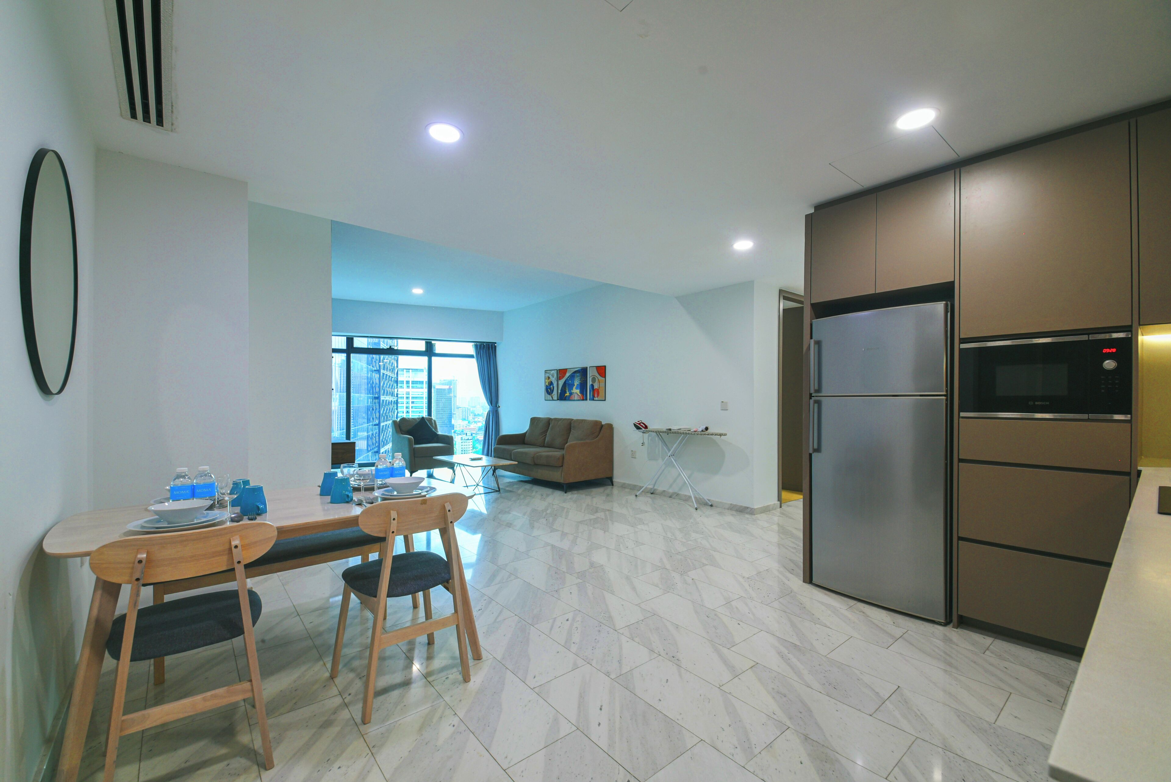 A modern kitchen with a built-in refrigerator and microwave, a dining area with a wooden table and chairs, and a living room with a sofa and a coffee table.