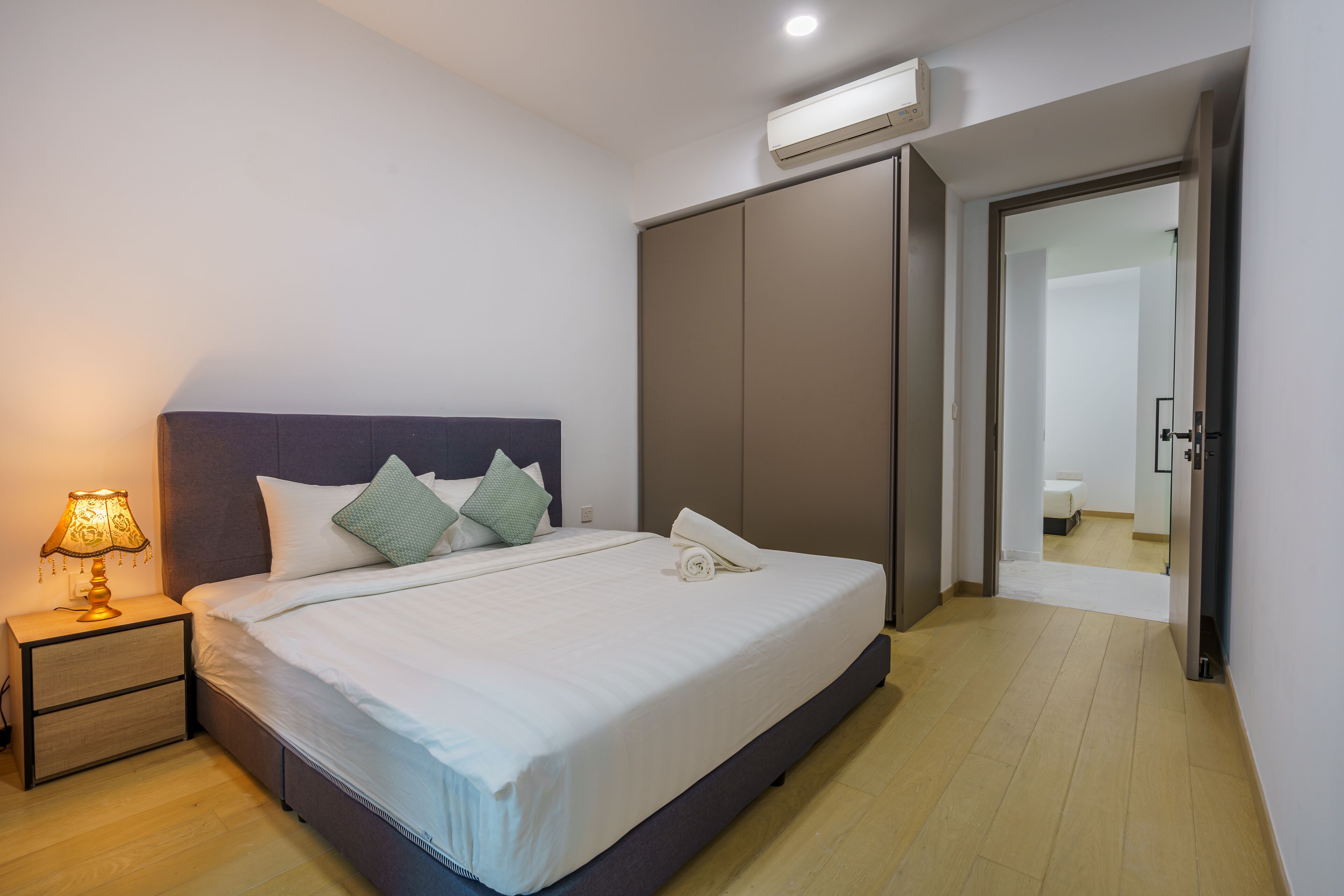 A neatly made bed with white linens and green pillows, a bedside table with a lamp, and a wardrobe with sliding doors.