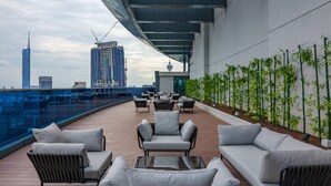 Una terraza en la azotea con mobiliario exterior, barandilla de cristal y vistas al horizonte de la ciudad.