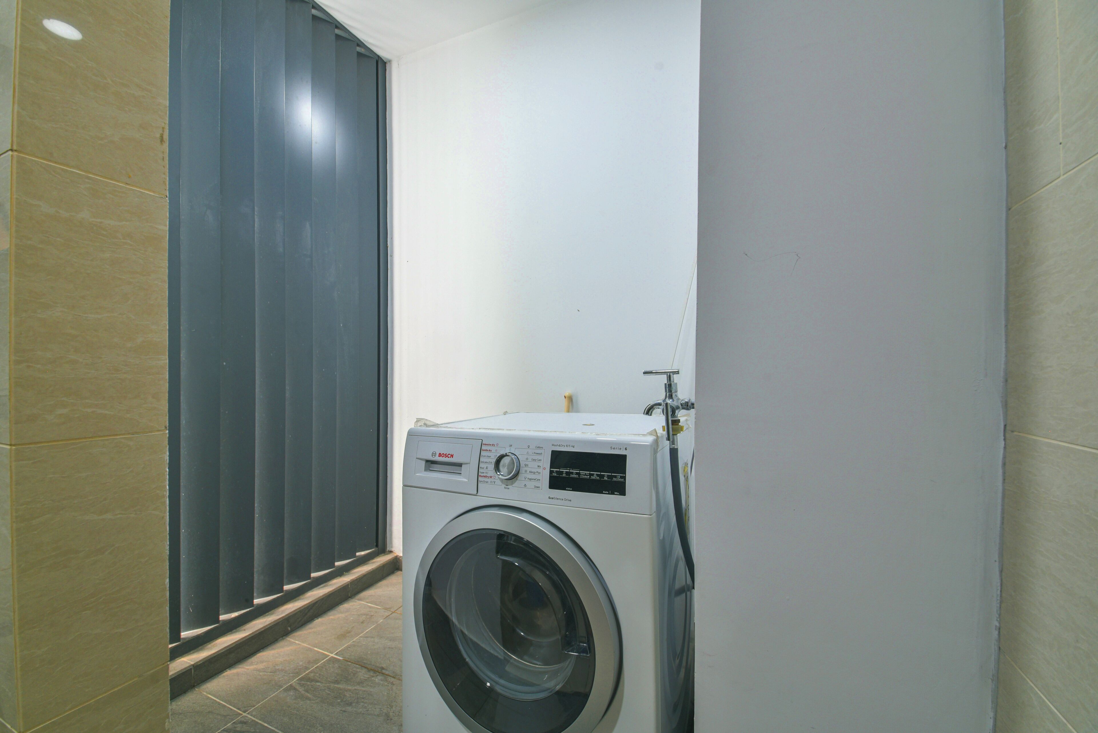 A compact, modern laundry room with a Bosch washing machine, a tiled floor, and a sliding door.