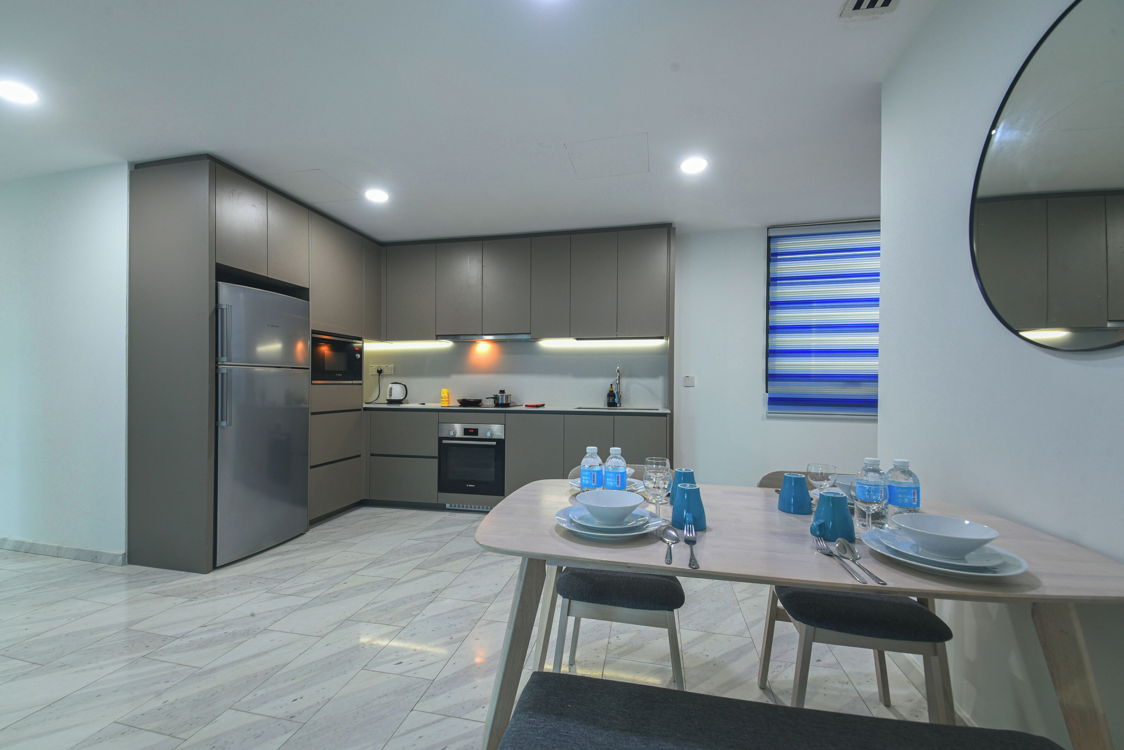 A modern kitchen with grey cabinets, a stainless steel refrigerator, and a dining area with a table set for two.