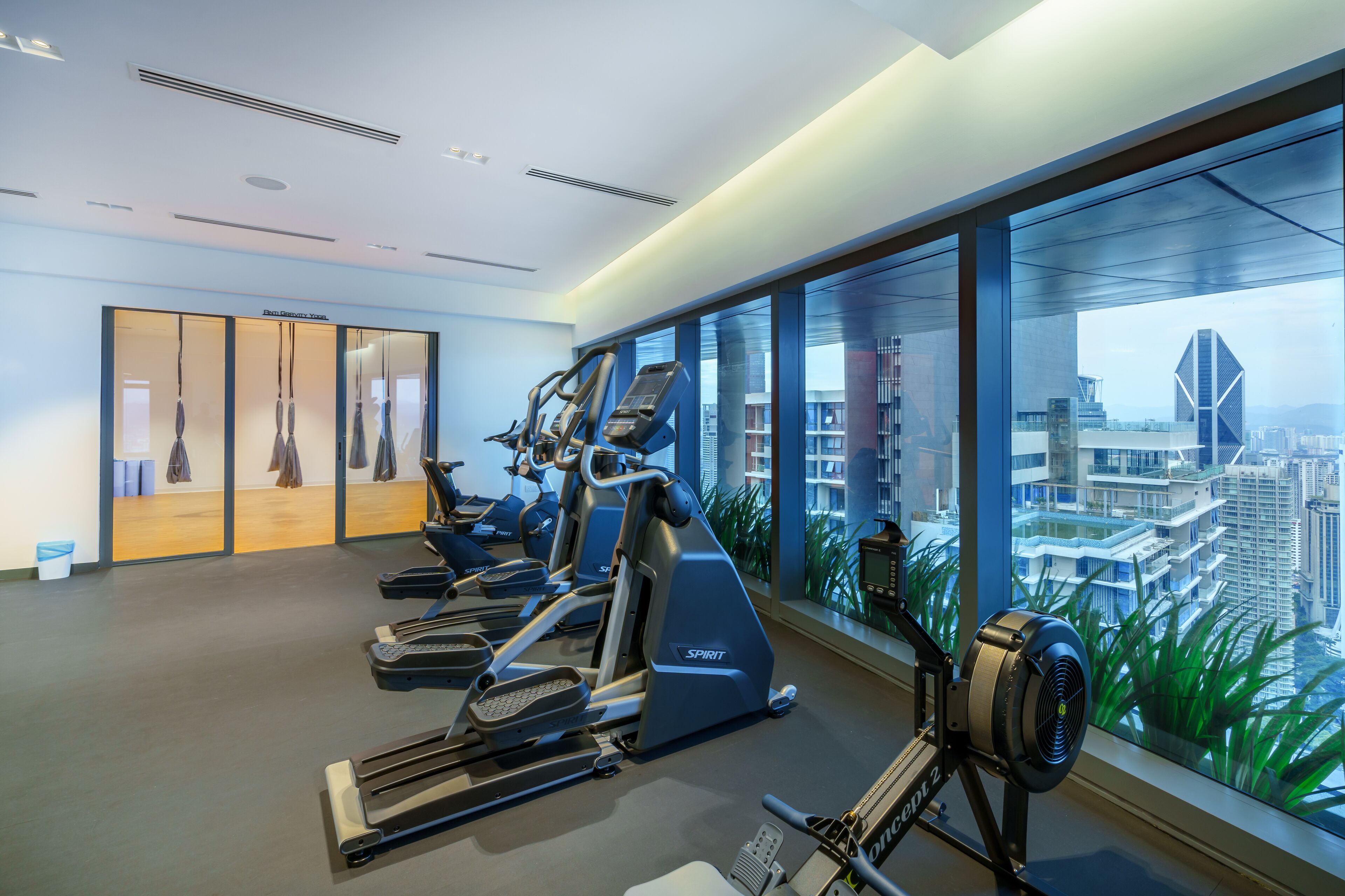 Ein modernes Fitnessstudio mit Laufbändern, Crosstrainern und Rudergeräten, mit großen Fenstern und Blick auf die Stadtlandschaft.