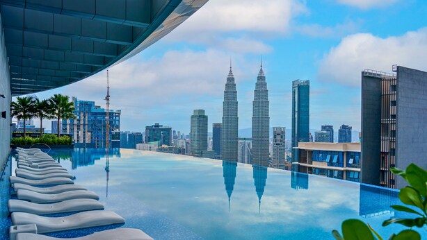 Una piscina infinita con vistas a las Torres Petronas, palmeras y edificios modernos.