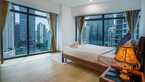 Una habitación de hotel moderna con una cama grande, una mesita de noche con lámpara y vistas a la ciudad a través de amplios ventanales.