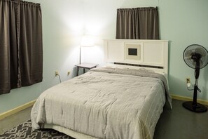 Une chambre à coucher avec un lit, une table de chevet, une lampe et un ventilateur sur pied.