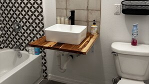 A bathroom with a white bathtub, a wooden vanity with a sink, and a toilet. - Remodeled quiet and spacious home. (Blythe)