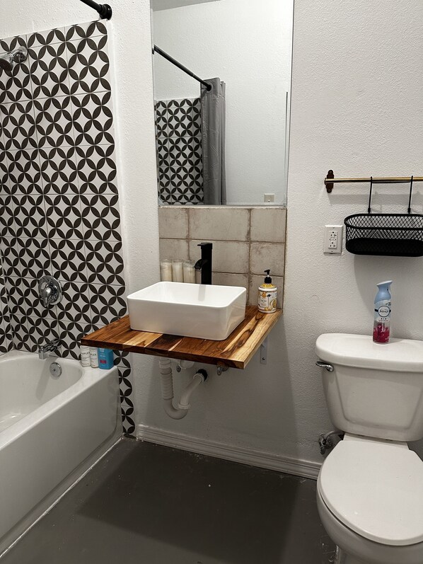 Et badeværelse med et hvidt badekar, et træbord med vask og et toilet.