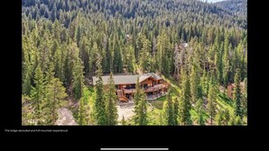 A lodge surrounded by dense forest, with a large wooden building featuring a porch and multiple windows.