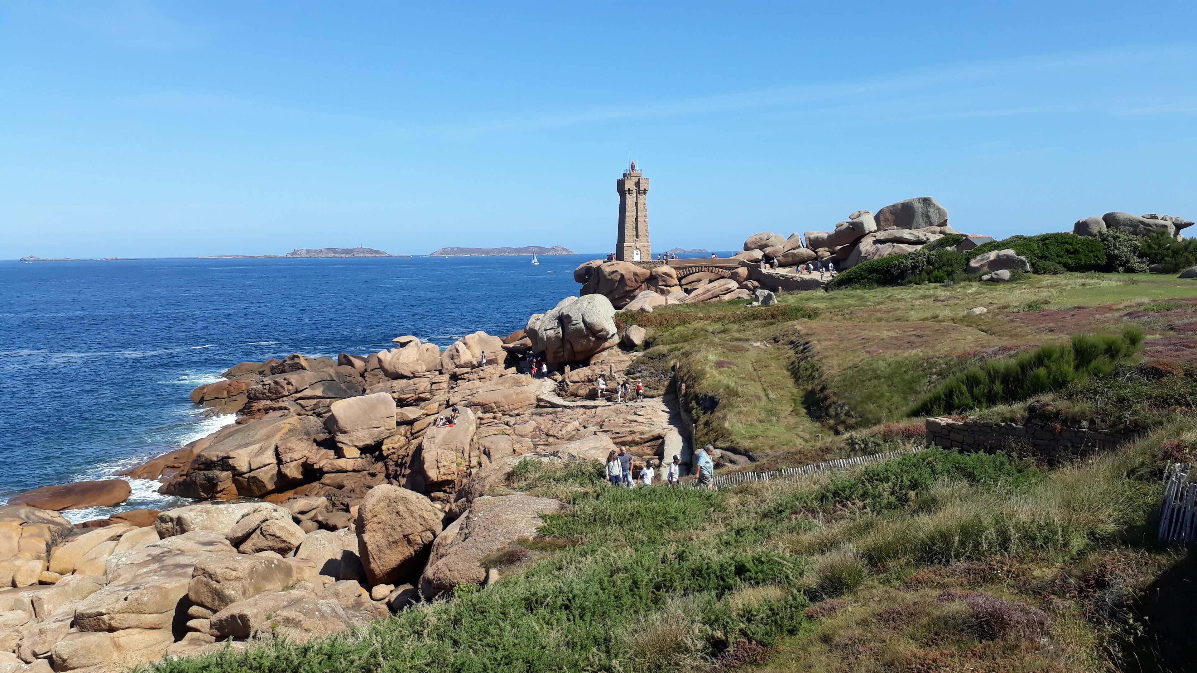 Paisatge costaner amb un far destacat, terreny rocos i vista clara del mar.