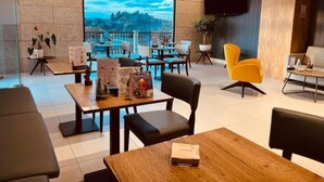 A modern restaurant with a large window offering a scenic view. Tables and chairs are arranged for dining. - Hotel Candor (A Lama)