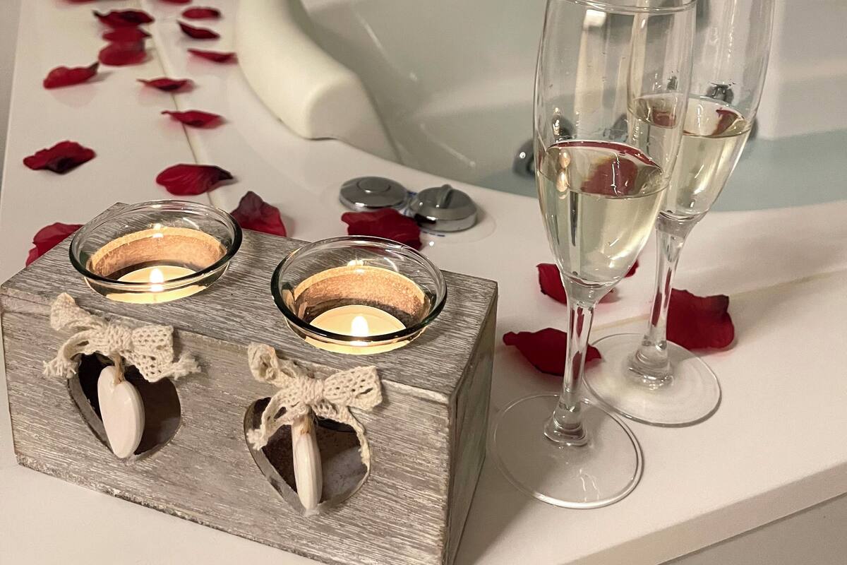 Ett badrum med ett badkar, tvÄ glas champagne, en ljusstake och en flaska badolja frÄn Candor.