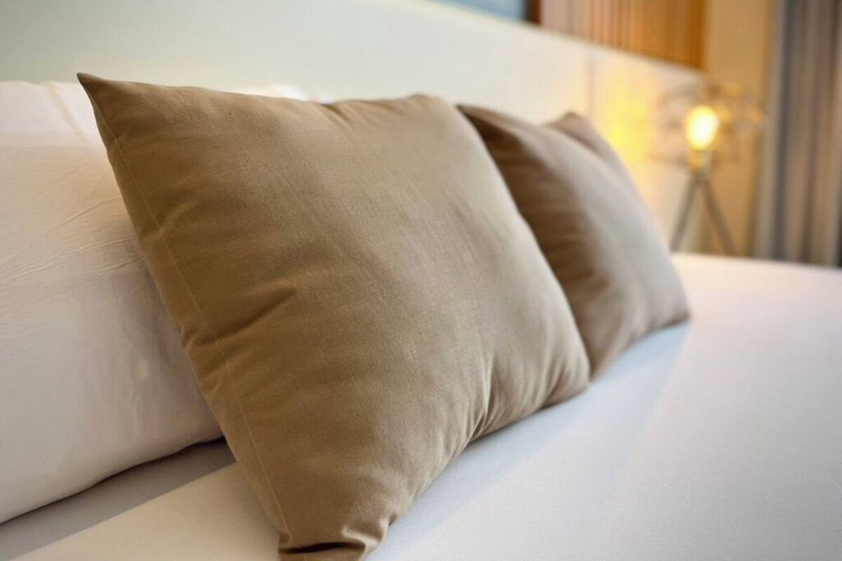En sÀng med tvÄ beige kuddar och en vit sÀnggavel i ett hotellrum.