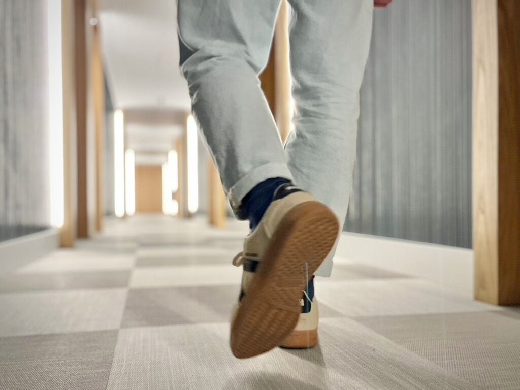 Una persona caminando por un pasillo con piso a cuadros y puertas de madera.