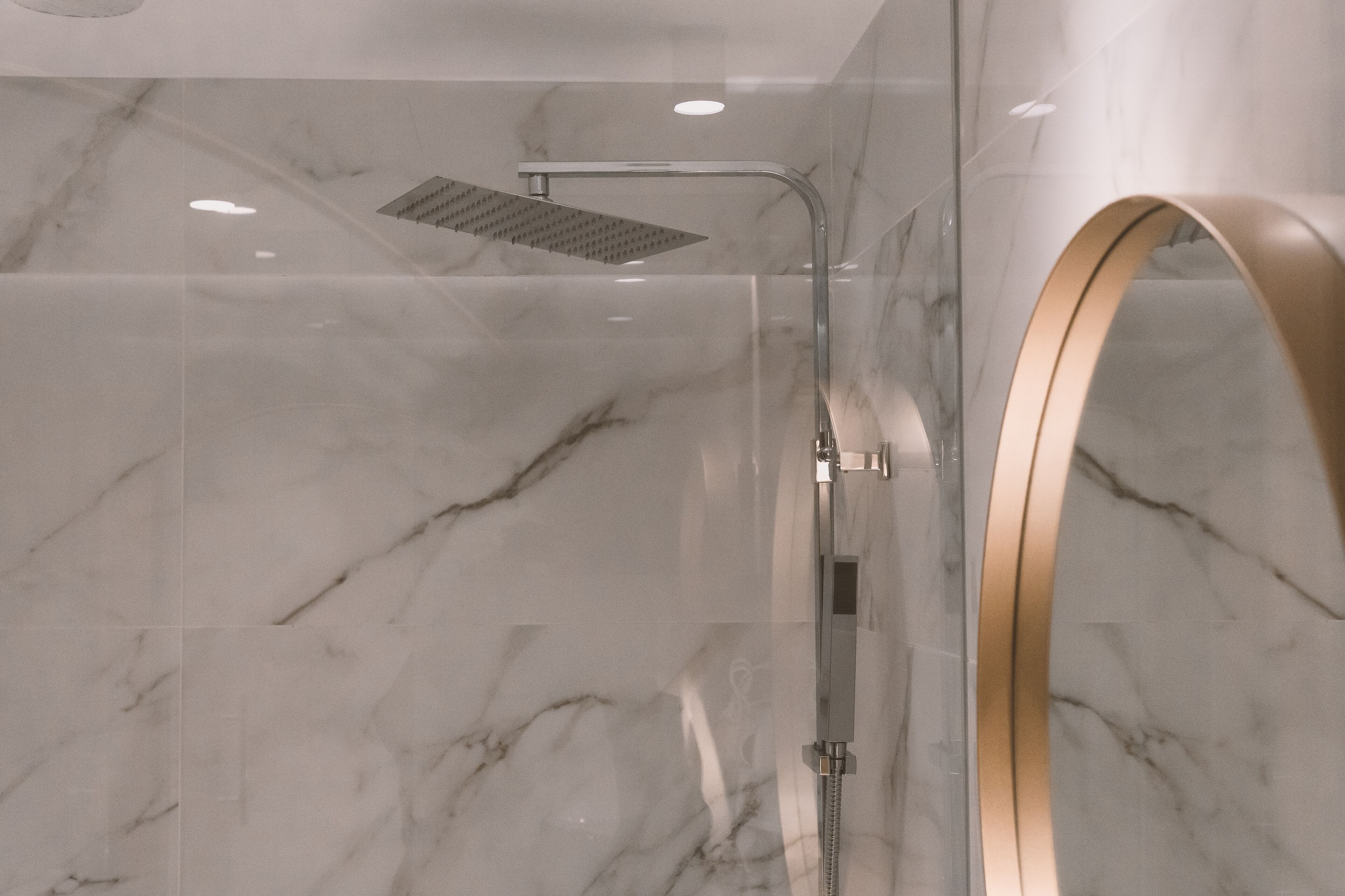 Une salle de bain moderne avec une douche à parois de verre, des murs en marbre et un miroir encadré d’or.