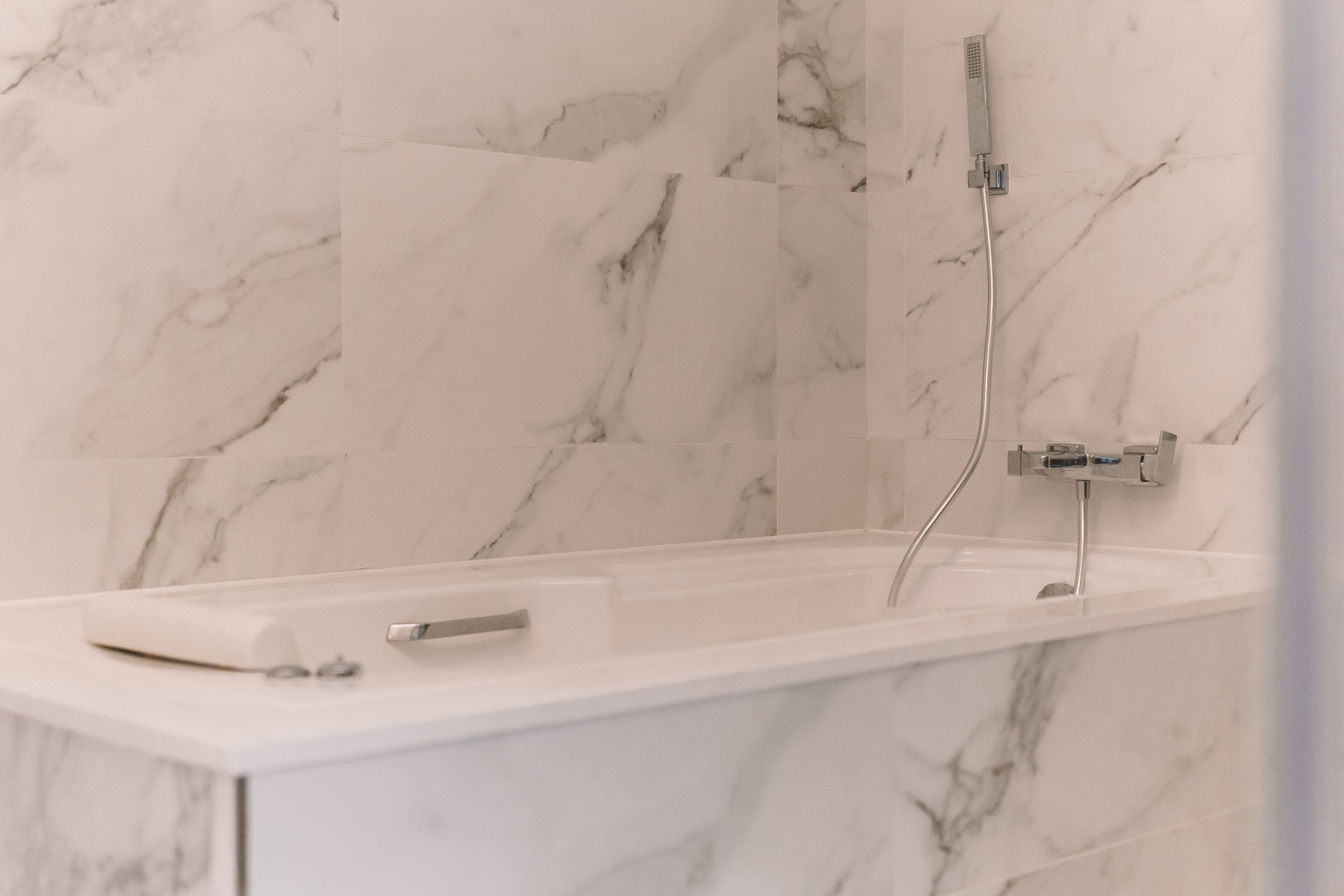 A modern bathroom with a marble wall, a bathtub, and a shower.