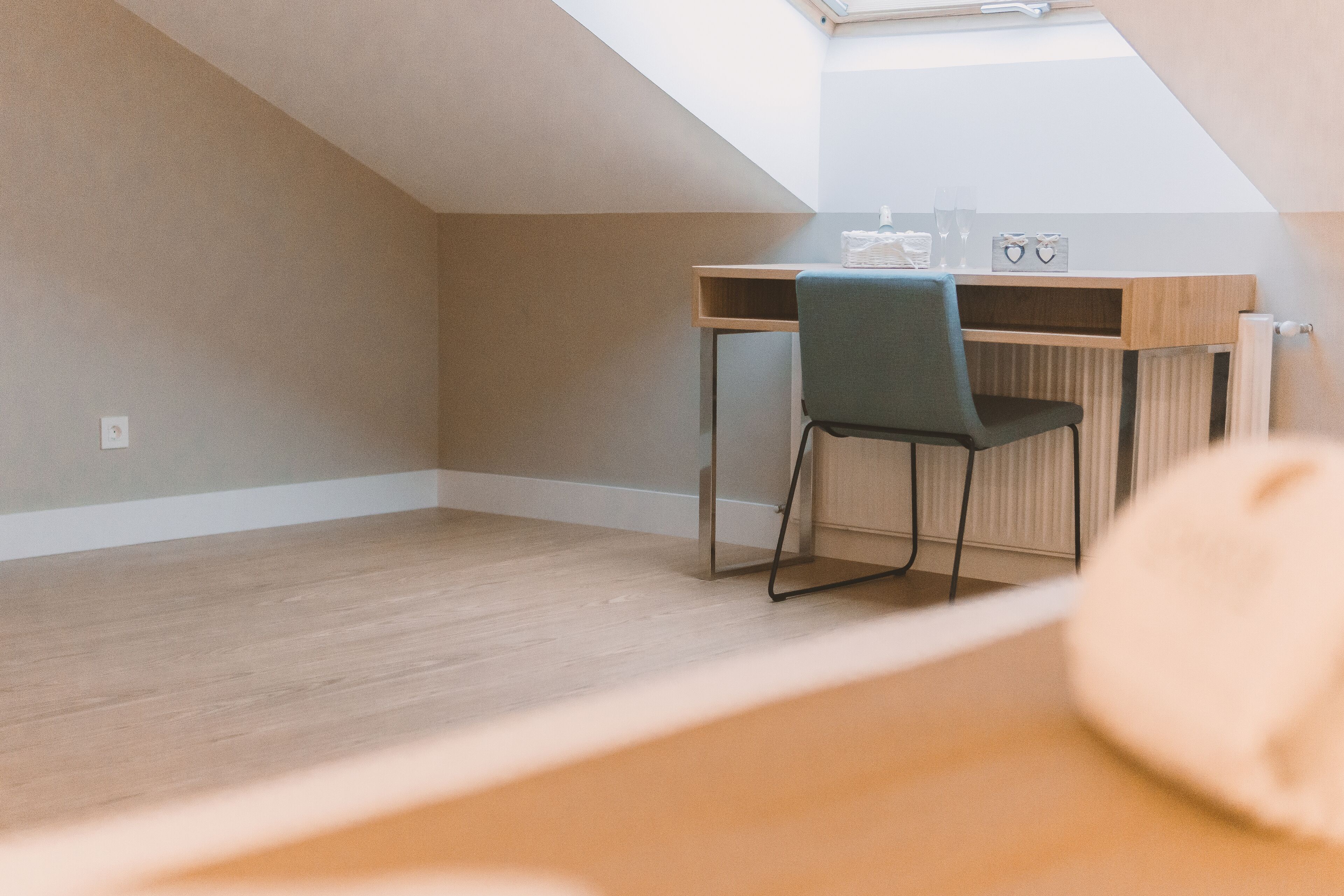 A room with a sloped ceiling, a desk with a chair, and a radiator.