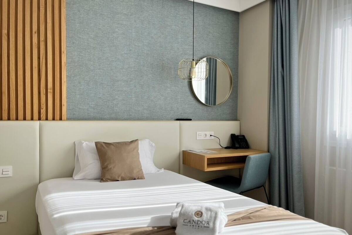 Ett hotellrum med en sÀng, ett skrivbord, en stol, en spegel och ett fönster med gardiner.