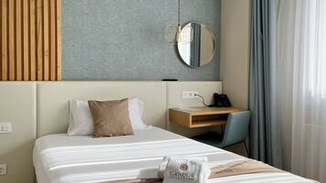 Habitación de hotel con cama, escritorio, silla, espejo y ventana con cortinas.