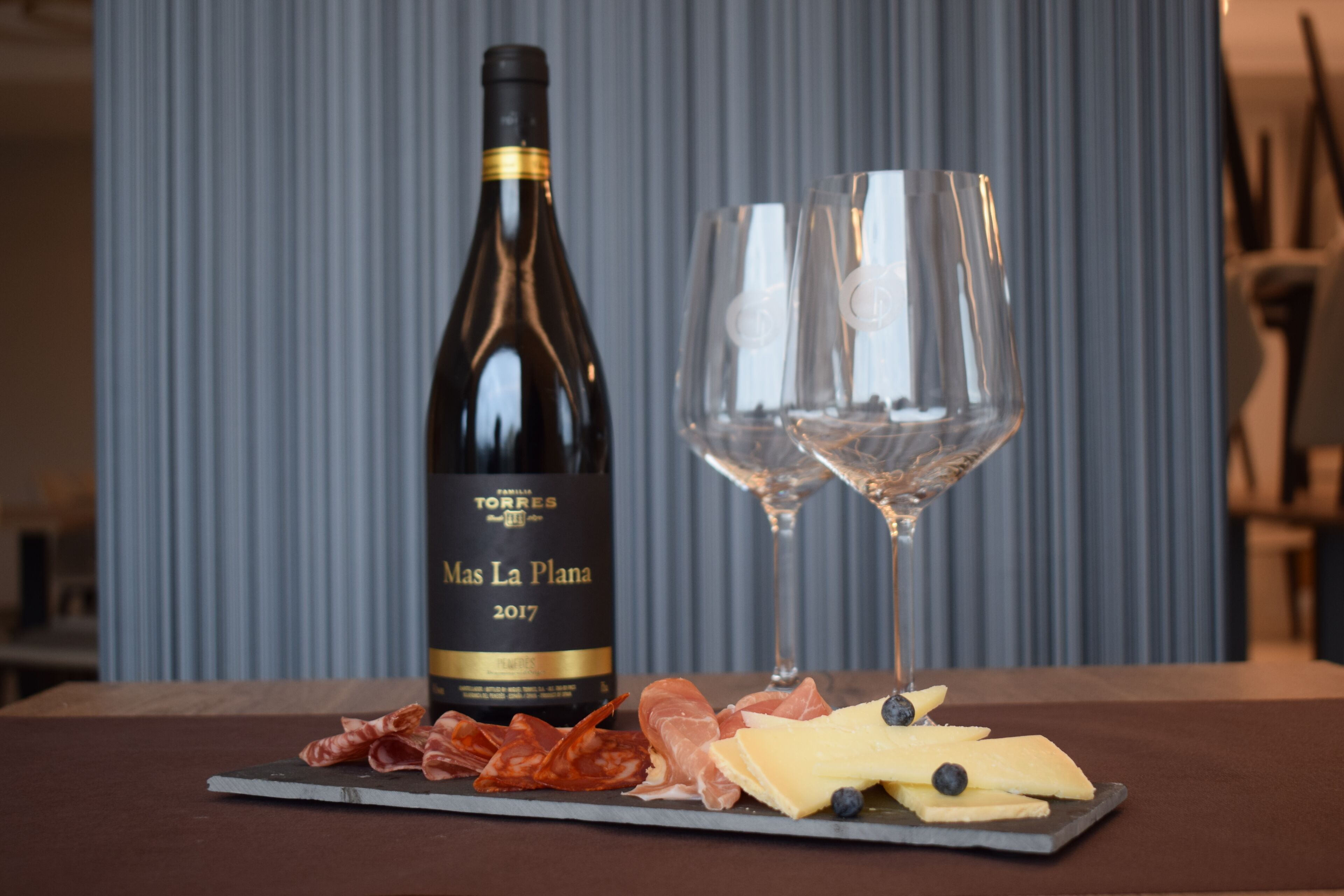 Una bottiglia di vino e due bicchieri su un tavolo con formaggi e salumi assortiti.