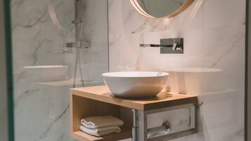 Une salle de bain moderne avec un mur en marbre, un meuble-lavabo en bois, un grand lavabo blanc et une cabine de douche en verre.