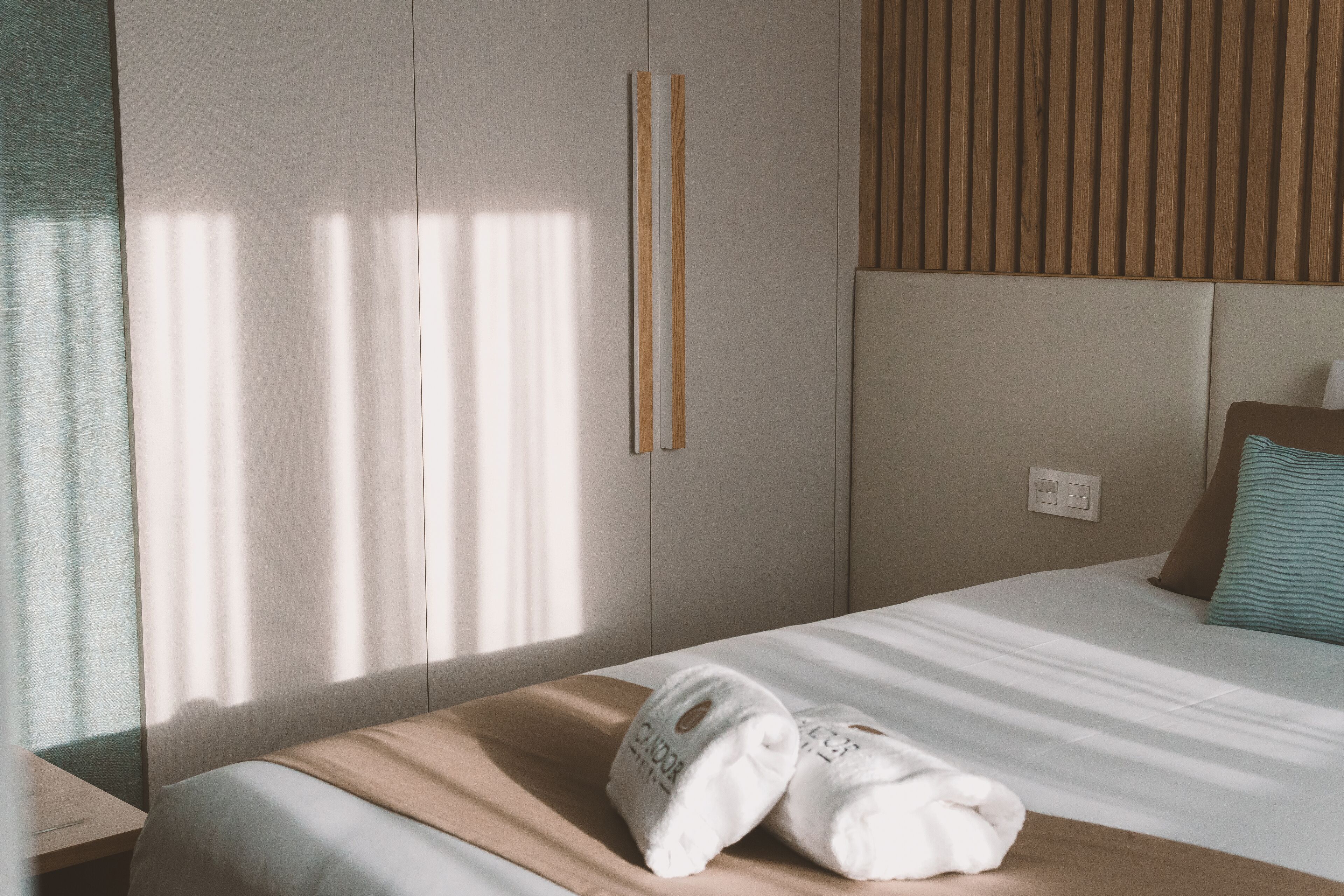 A neatly made bed with a white and beige bedspread, a pair of white towels, and a single pillow.