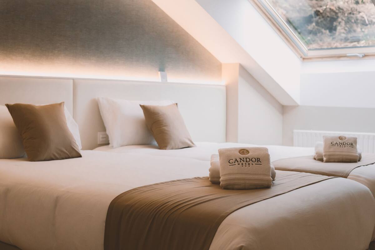 Ett hotellrum med en stor sÀng, tvÄ kuddar, en sÀnggavel och ett takfönster.