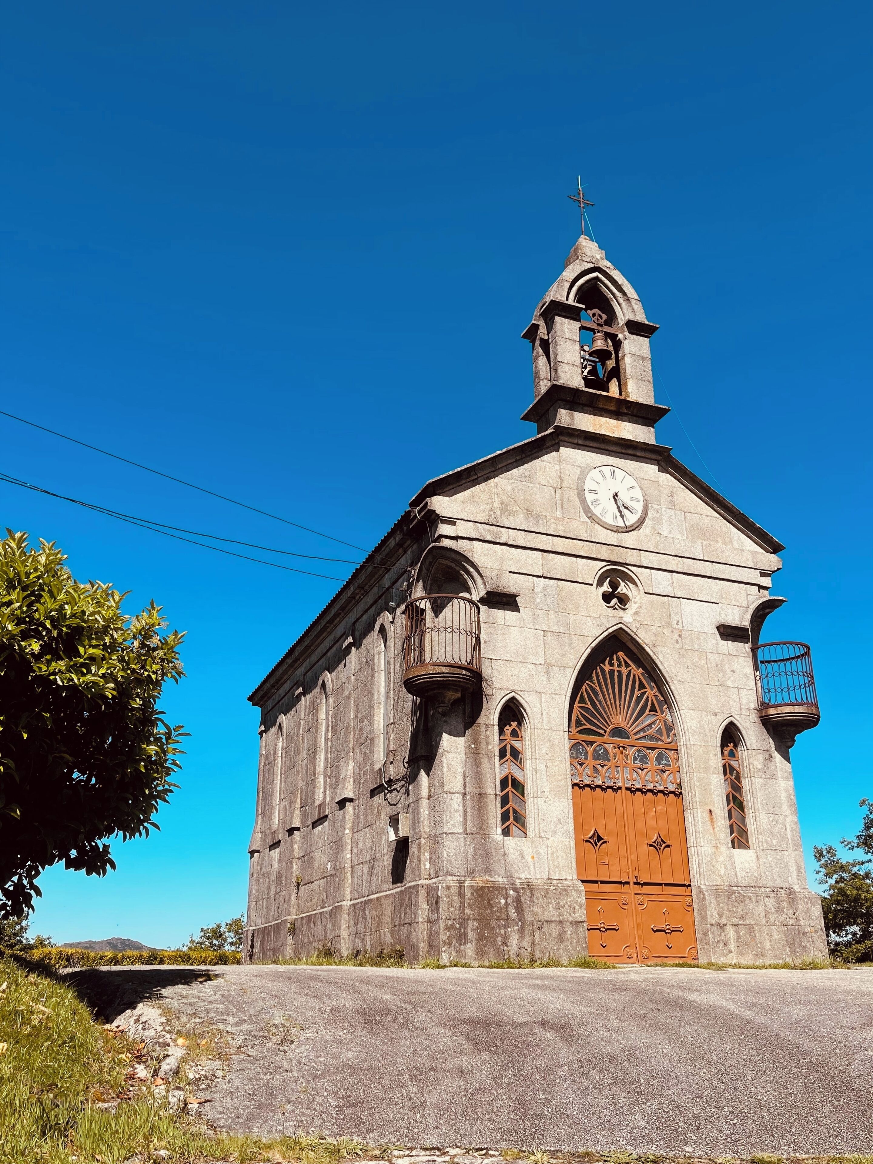 Una iglesia de piedra histórica con una torre de reloj, ventanas en arco y una puerta de madera.