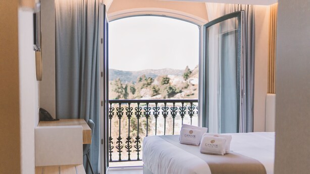 A hotel room with a bed, a desk, and a balcony with a view of the mountains. - Hotel Candor (A Lama)