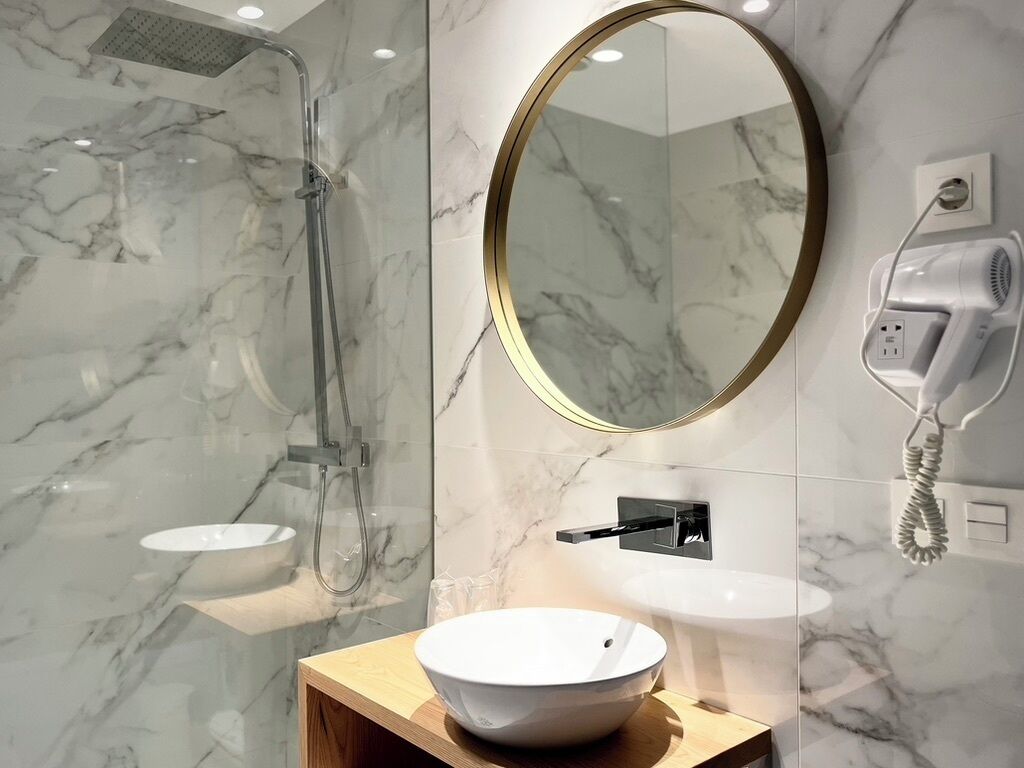 Un baño moderno con ducha de mármol, espejo redondo y lavamanos blanco.
