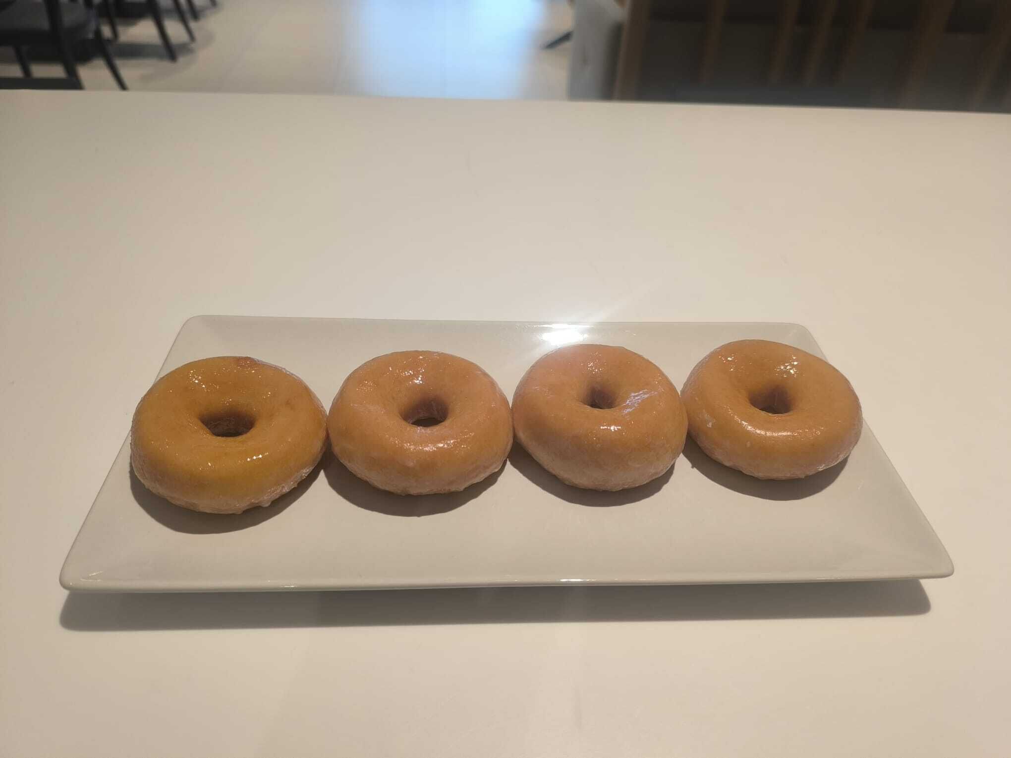 A white plate with four glazed donuts on a white table.