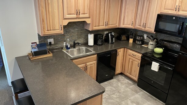A modern kitchen with wooden cabinets, a granite countertop, a dishwasher, a stove, and a microwave. - Ski condo close to multiple resorts (Mendon)