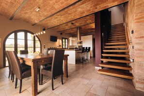 A modern kitchen with a central island, a dining area with a wooden table and chairs, and a staircase with wooden steps. - PENDOLINO — LUXURY COTTAGE WITH POOL & BREATHTAKING VIEW (Ghizzano)