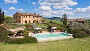 Une grande maison avec une piscine, entourée d’une végétation luxuriante et de collines.