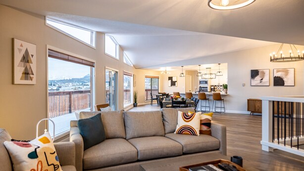 A spacious living area with a sofa, coffee table, and artwork. A balcony with a view of a snowy landscape is visible. - Gorgeous Retreat with Mountain Views, Open Living, Game Room, Hot Tub (Glenwood Springs)