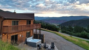 A wooden cabin with a balcony, a hot tub, and outdoor seating. - Gorgeous Retreat with Mountain Views, Open Living, Game Room, Hot Tub (Glenwood Springs)