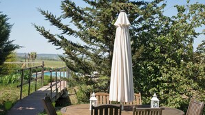 A wooden table with chairs and a white umbrella in a garden setting with a view of a pool and hills. - Air-conditioned gîte: a swimming pool just for you, superb view of the Cévennes  (Blauzac)