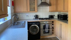 Een kleine keuken met houten kastjes, een ingebouwde wasmachine en een kookplaat.