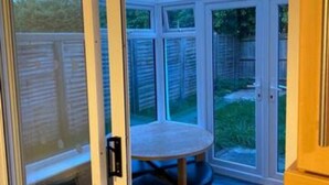 Een glazen deur die uitkomt op een terras met een ronde tafel en stoelen.